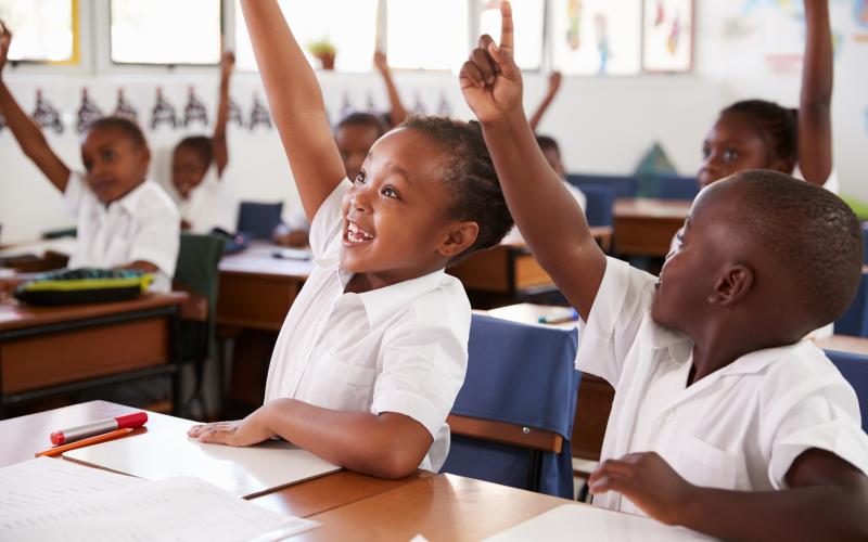 Happy children raising their hands in class